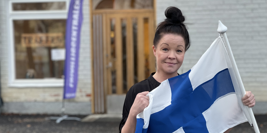 Sandra Kuismanen framför entrén till Frivillgcentralen med en finsk flagga i handen.